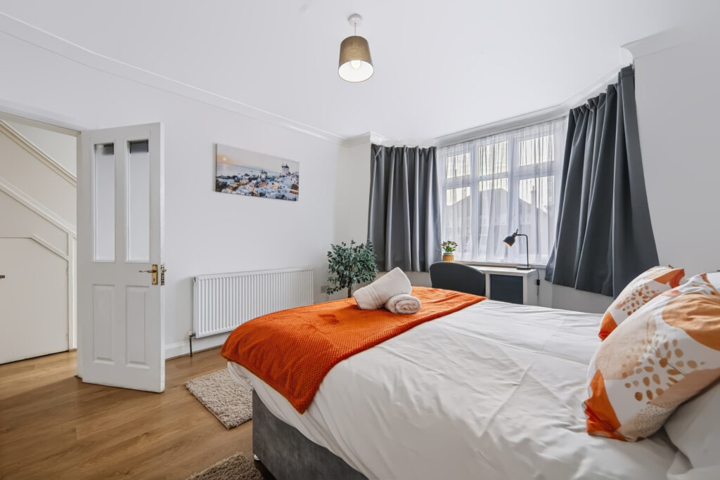 Bright bedroom with orange throw, desk, and gray curtains