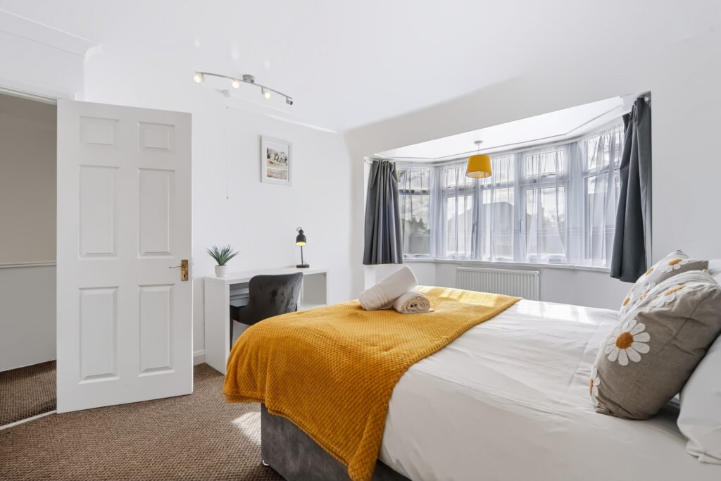 Bright bedroom with mustard throw, desk, and bay window