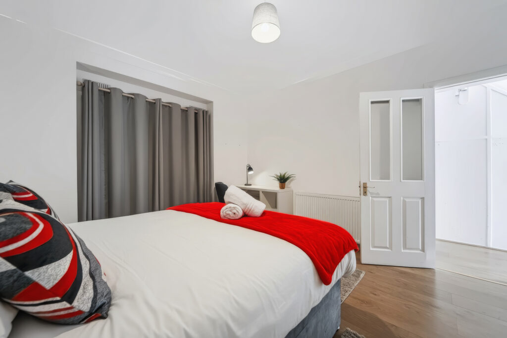 Bright bedroom with red throw, gray curtains, and desk