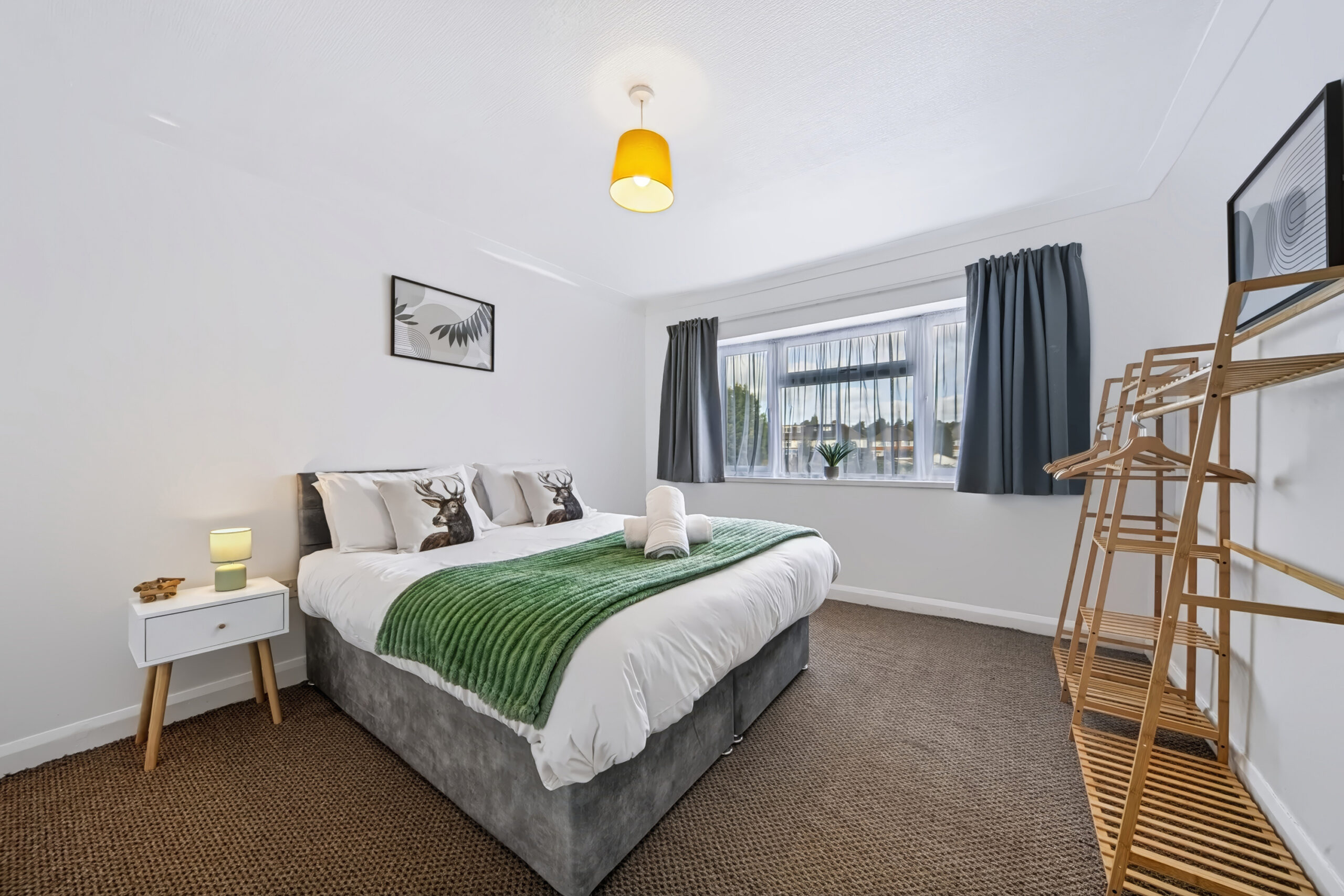 Bright modern bedroom with green throw and wooden clothes rack