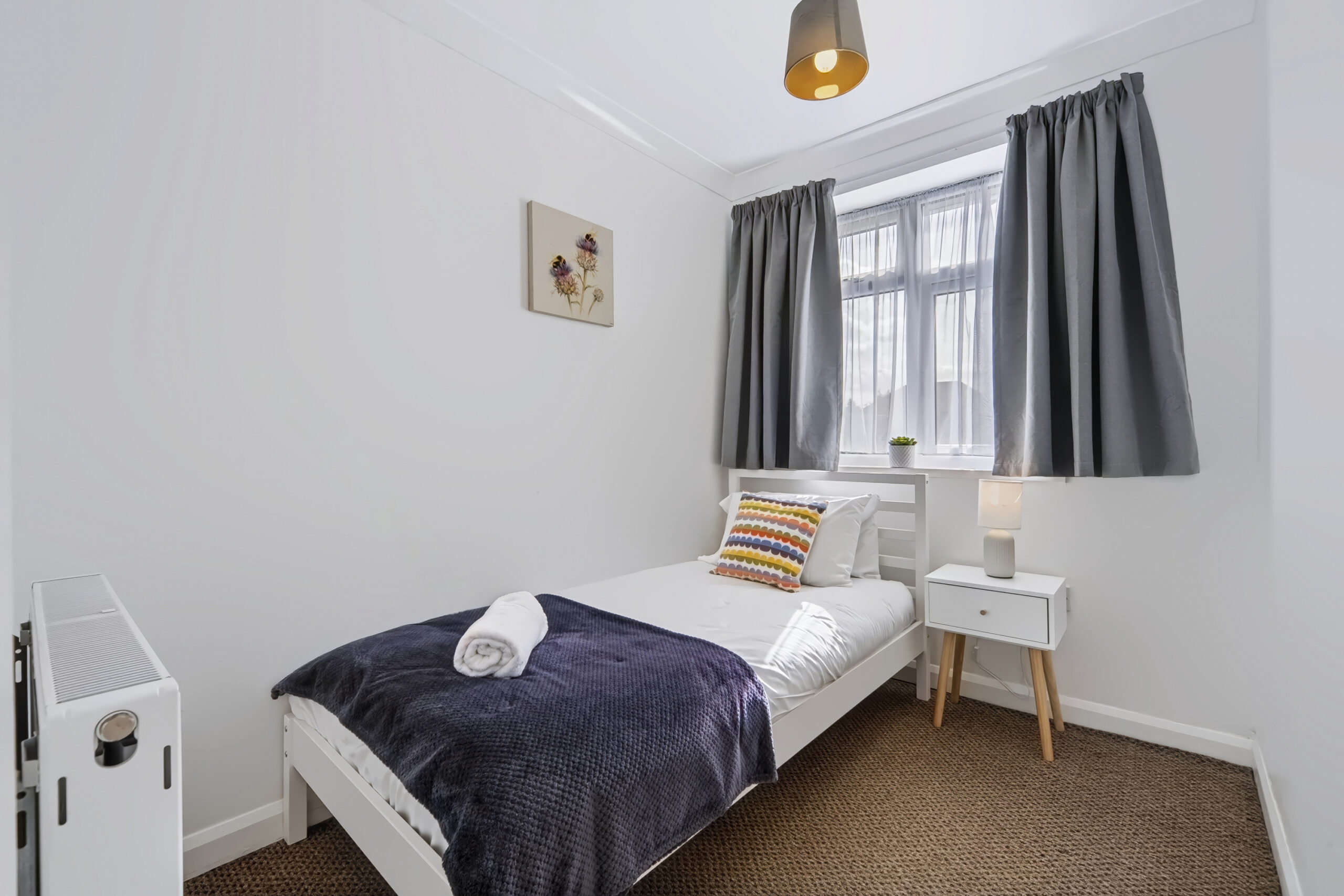 Bright single bedroom with gray curtains and navy blanket