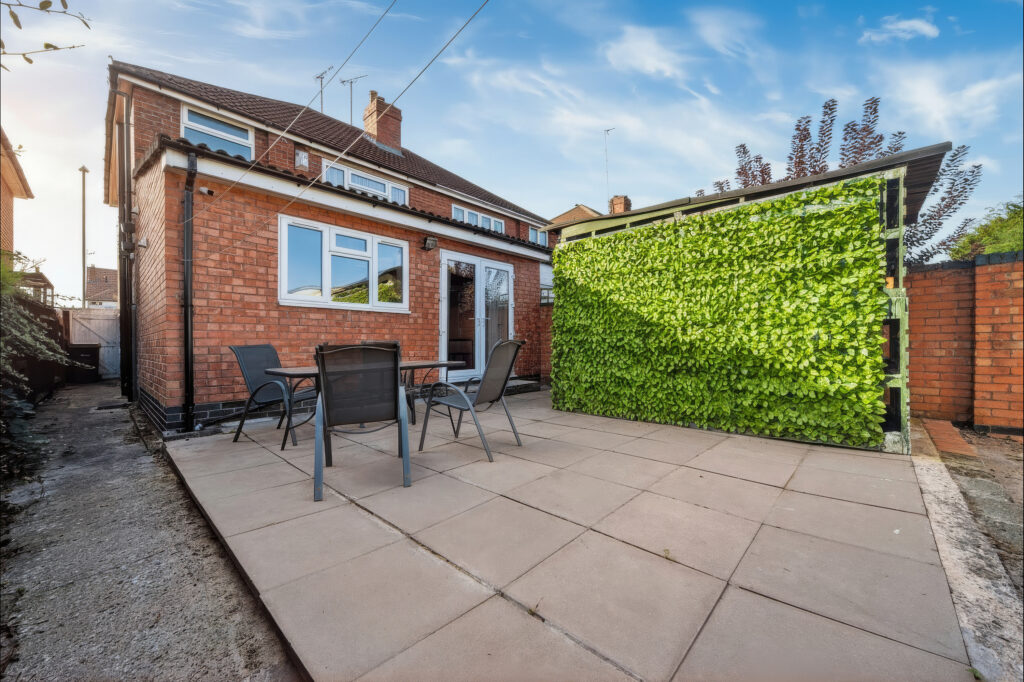 Brick house patio with chairs and leafy privacy hedge